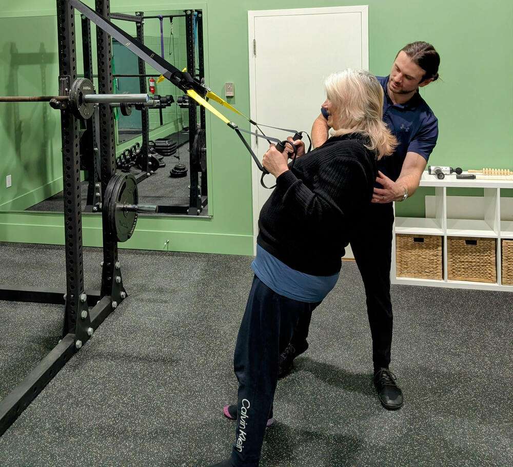 Home 7 Senior patient performing TRX row exercise with guidance from physiotherapist John Thornton at LiveRight Physiotherapy in Burlington ON 1
